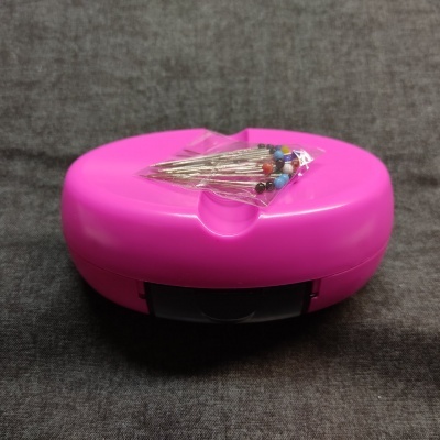 Caixa de plástico rosa com alfinetes coloridos num saco plástico em cima