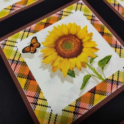 Pano decorativo com girassol e borboleta em moldura quadriculada colorida.