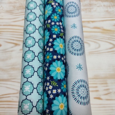 Três rolos de tecido coloridos com padrões geométricos e florais sobre madeira clara