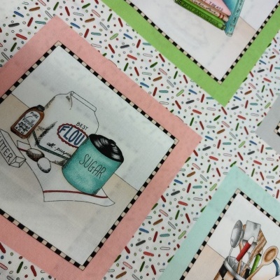 Tecido decorativo com desenhos de produtos e utensílios de cozinha em molduras coloridas sobre fundo branco com padrão colorido