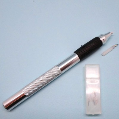 Caneta técnica prateada com pega preta e caixa com pontas de reposição sobre fundo azul