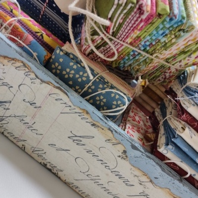 Pilhas de tecidos coloridos com padrões variados e cordões brancos sobre superfície com escrita manuscrita.