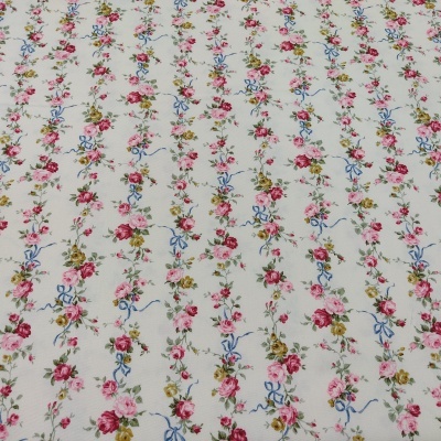 Tecido branco com pequenas flores coloridas e laços azuis em riscas verticais.