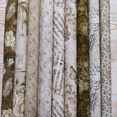 Rolos de tecido com padrões florais, musicais e manuscritos em tons neutros e verdes