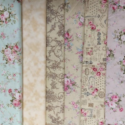 Rolos de tecido com estampados florais e padrões decorativos em tons pastel.