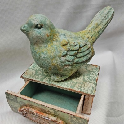 Escultura de pássaro verde sobre móvel decorativo com gaveta aberta