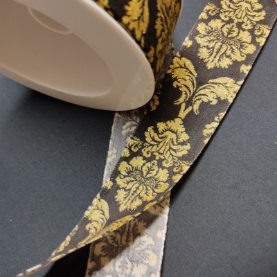 Rolo de fita decorativa preta com padrão floral dourado em tecido.