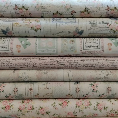 Rolos de tecido estampado com motivos florais e botões, em tons pastel, empilhados.