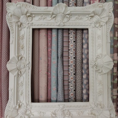 Moldura decorativa branca com tecidos coloridos em padrão pastel ao fundo