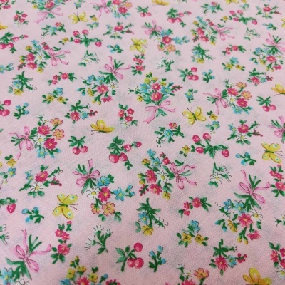 Tecido rosa claro com padrão floral colorido e pequenos elementos como laços e cerejas