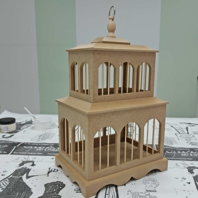 Estrutura decorativa em madeira crua com janelas arqueadas sobre mesa com pano decorativo