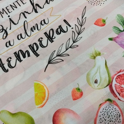 Tecido com padrão de frutas coloridas e texto em português em fundo listrado rosa claro