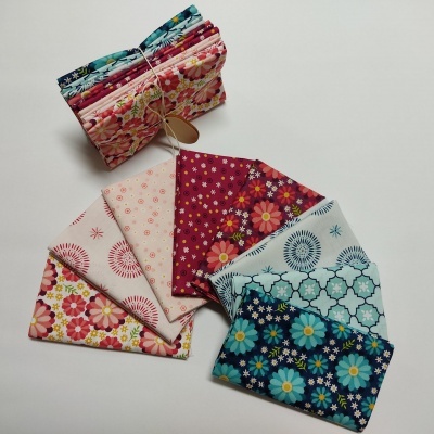 Conjunto de seis tecidos florais coloridos sobre mesa branca com outro conjunto empilhado ao fundo