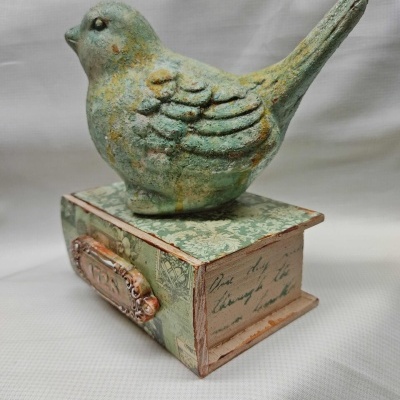 Escultura decorativa de pássaro verde sobre caixa decorada