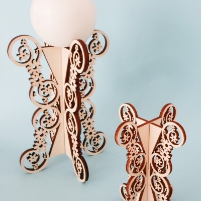 Suportes decorativos em madeira em forma de ursinhos com padrões recortados, um com vela branca redonda, sobre fundo azul claro.