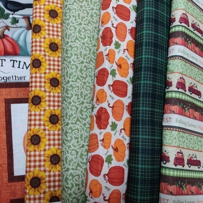 Tecidos com estampas de girassóis, abóboras, xadrez verde e frases sobre folhas caídas.