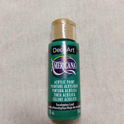 Frasco de tinta acrílica DecoArt Americana verde com tampa dourada sobre tecido bege