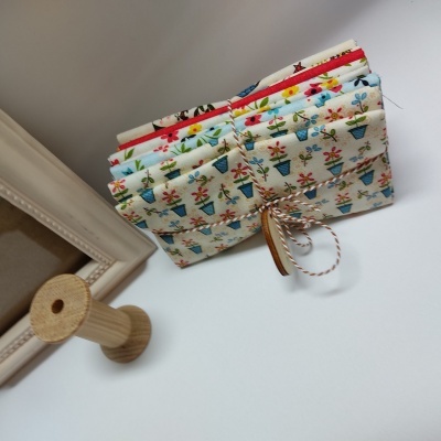 Três bolsas de tecido com estampas de vasos de flores e cordão trançado sobre superfície branca