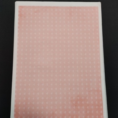 Bloco de papel rosa com padrão branco em embalagem plástica sobre superfície preta