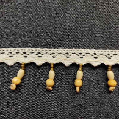 Franja decorativa de renda bege com contas de madeira sobre tecido azul-escuro