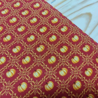 Tecido com padrão de abóboras amarelas e laranjas sobre fundo vermelho