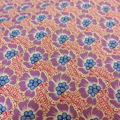 Tecido com padrão floral lilás, azul e vermelho sobre fundo rosa
