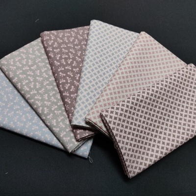 Seis tecidos dobrados com padrões florais e geométricos em tons pastel sobre fundo preto