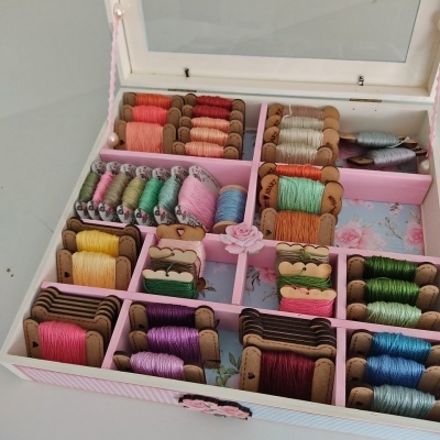 Caixa de madeira rosa organizada com carretéis de linha colorida