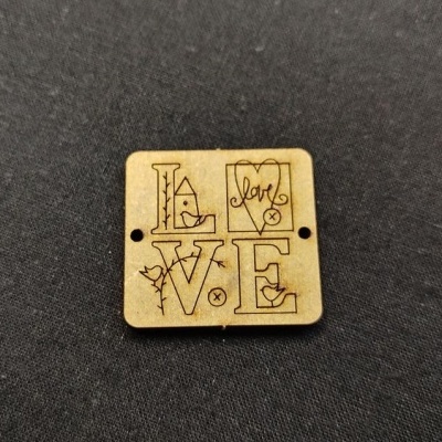 Peça quadrada em madeira clara gravada com a palavra LOVE e elementos decorativos sobre fundo preto