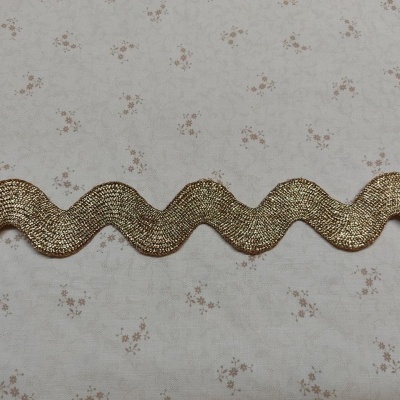 Fitilho dourado ondulado sobre tecido branco com flores pequenas cor de rosa