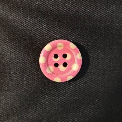 Botão rosa com bolinhas brancas e quatro furos no centro