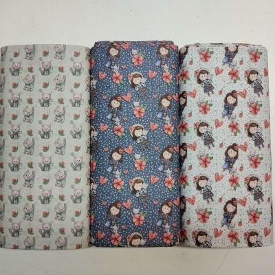 Três rolos de tecido com estampados infantis variados em fundo cinza claro, azul escuro e branco.