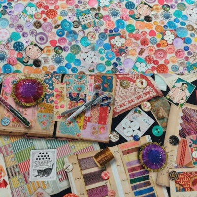 Mesa cheia de botões coloridos, linhas, cadernos, alfineteiros e artigos de costura