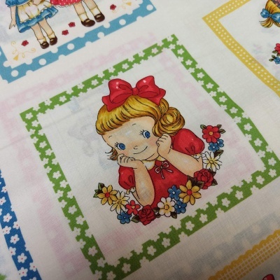 Tecido com desenhos infantis de menina loira e flores em quadrados coloridos