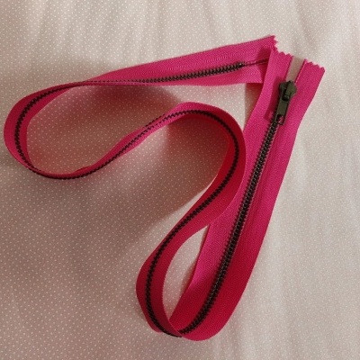 Fecho éclair rosa com dentes metálicos pretos sobre tecido bege com pontos brancos