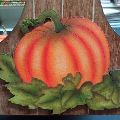 Placa decorativa em madeira com pintura de abóbora laranja e folhas verdes