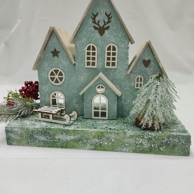 Decoração natalícia em madeira verde com casa, trenó e árvore com neve