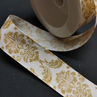 Rolo de fita decorativa branca com padrão floral dourado sobre superfície escura