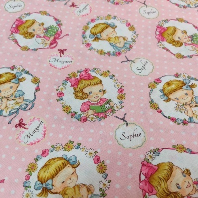 Pano rosa com bolinhas brancas e desenhos de meninas loiras em molduras florais com nomes Sophie e Margaret.