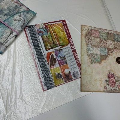 Dois envelopes decorativos florais e uma folha com texto 'STONE PAPER' sobre superfície branca