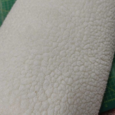 tecido branco pelúcia sherpa com padrão irregular sobre superfície verde com linhas de grade