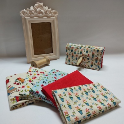 tecidos coloridos com padrão floral e carteira com padrão de vasos de flores sobre superfície branca junto a porta-retrato ornamentado