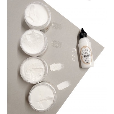 Quatro frascos abertos com tintas brancas e um frasco fechado com tampa preta sobre fundo cinzento.