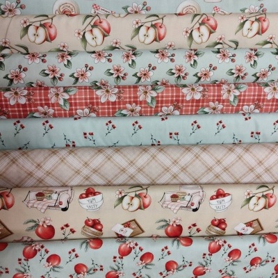 Tecidos com padrões de maçãs, flores, xadrez e texto 'YUM TASTY' em cores suaves.