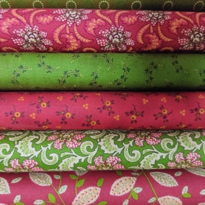 Tecidos coloridos com padrões florais e geométricos em verde e rosa empilhados