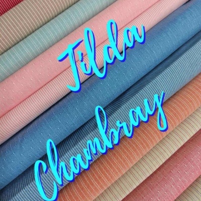 Tecidos dobrados em cores pastel com texturas e padrões variados e texto Tilda Chambray