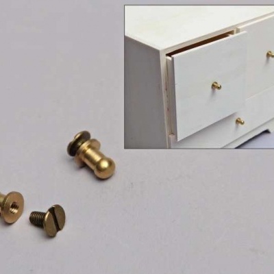 Parafusos dourados ao lado de uma gaveta branca com puxadores dourados