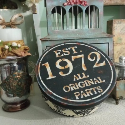 Objeto decorativo redondo com texto EST. 1972 ALL ORIGINAL PARTS e padrão floral preto e branco