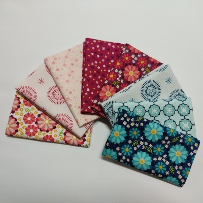 Seis tecidos dobrados com padrões florais e geométricos em várias cores sobre fundo branco.