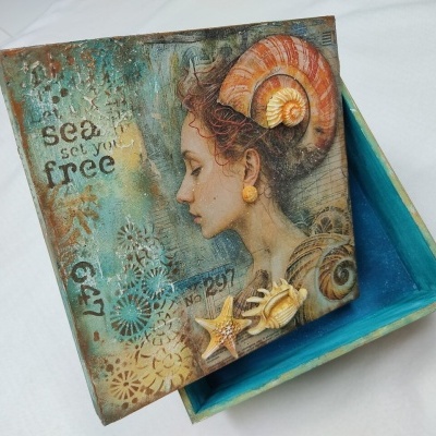 Caixa decorativa azul com tampa ilustrada e texto 'sea set you free'.
